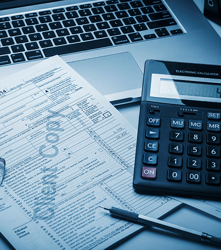 A white desktop with a laptop, calculator and tax form on top of it.